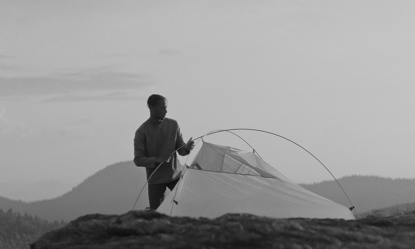 Man putting up tent on mountaintop.