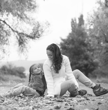 Mother and daughter sitting back-to-back smiling outside during Fall.