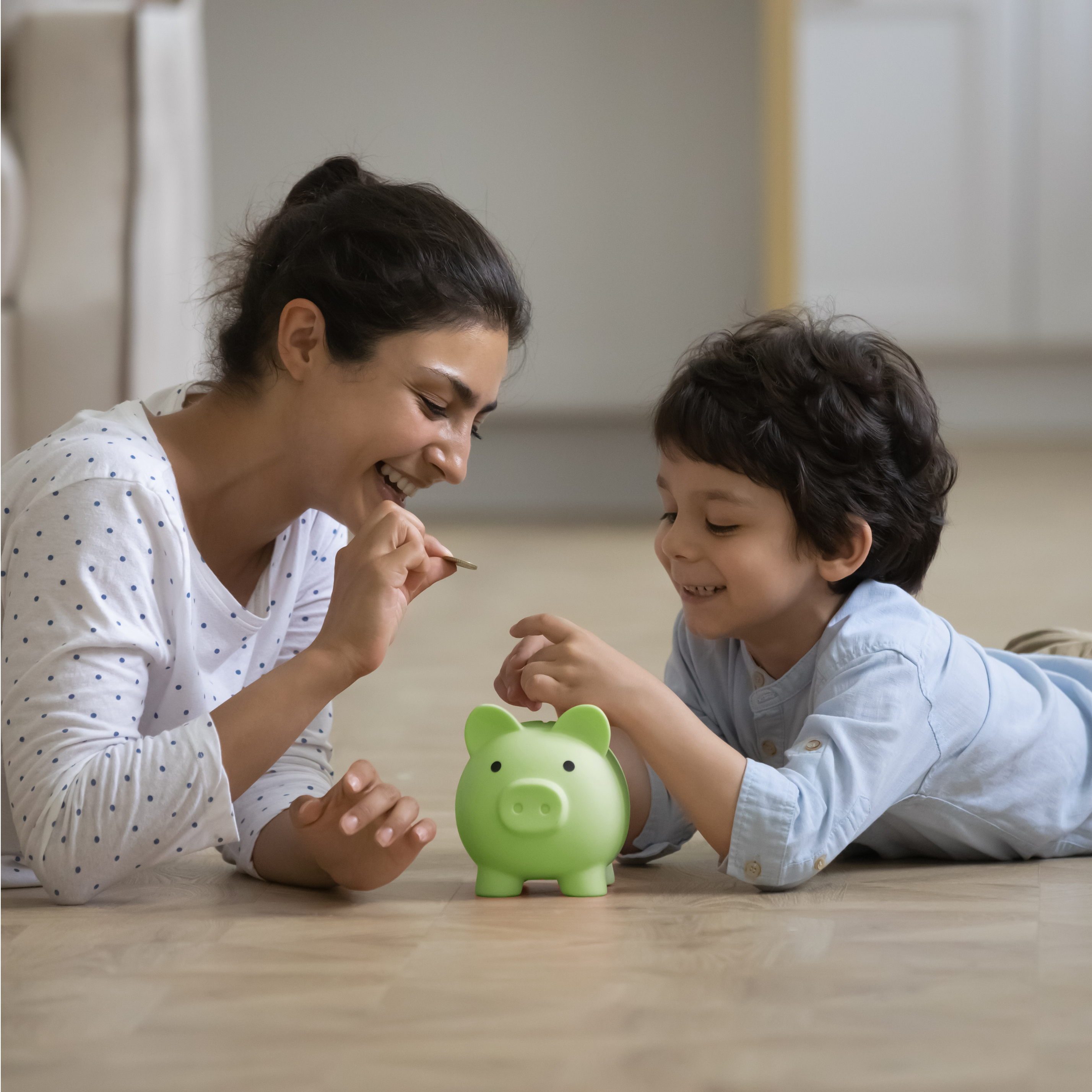 Mother and son adding coins to green piggybank.