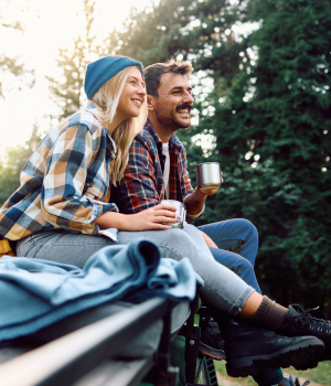 Couple drinking coffee and sitting on vehicle roof in nature.