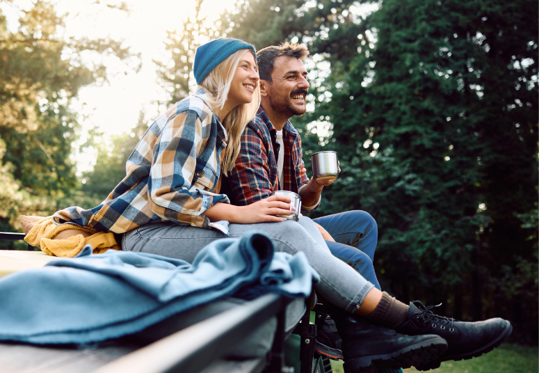 Couple drinking coffee and sitting on vehicle roof in nature.