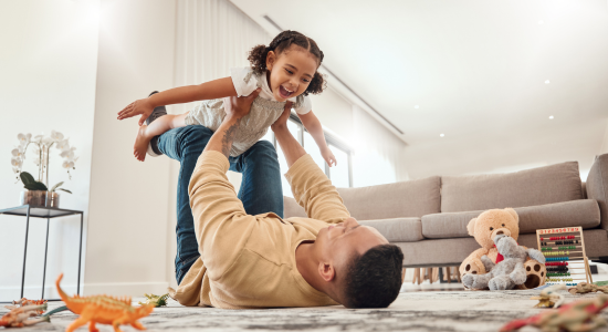 Dad playing with daughter on floor of home.