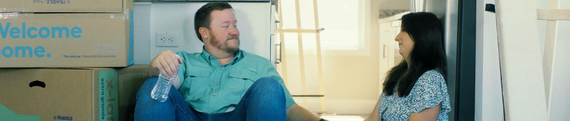 Couple sitting on floor smiling in new home.