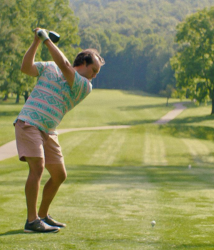 Man on golf course teeing off.