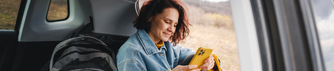 Woman sitting in open car trunk looking at phone.