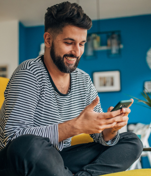 Man sitting on couch and smiling while using phone.